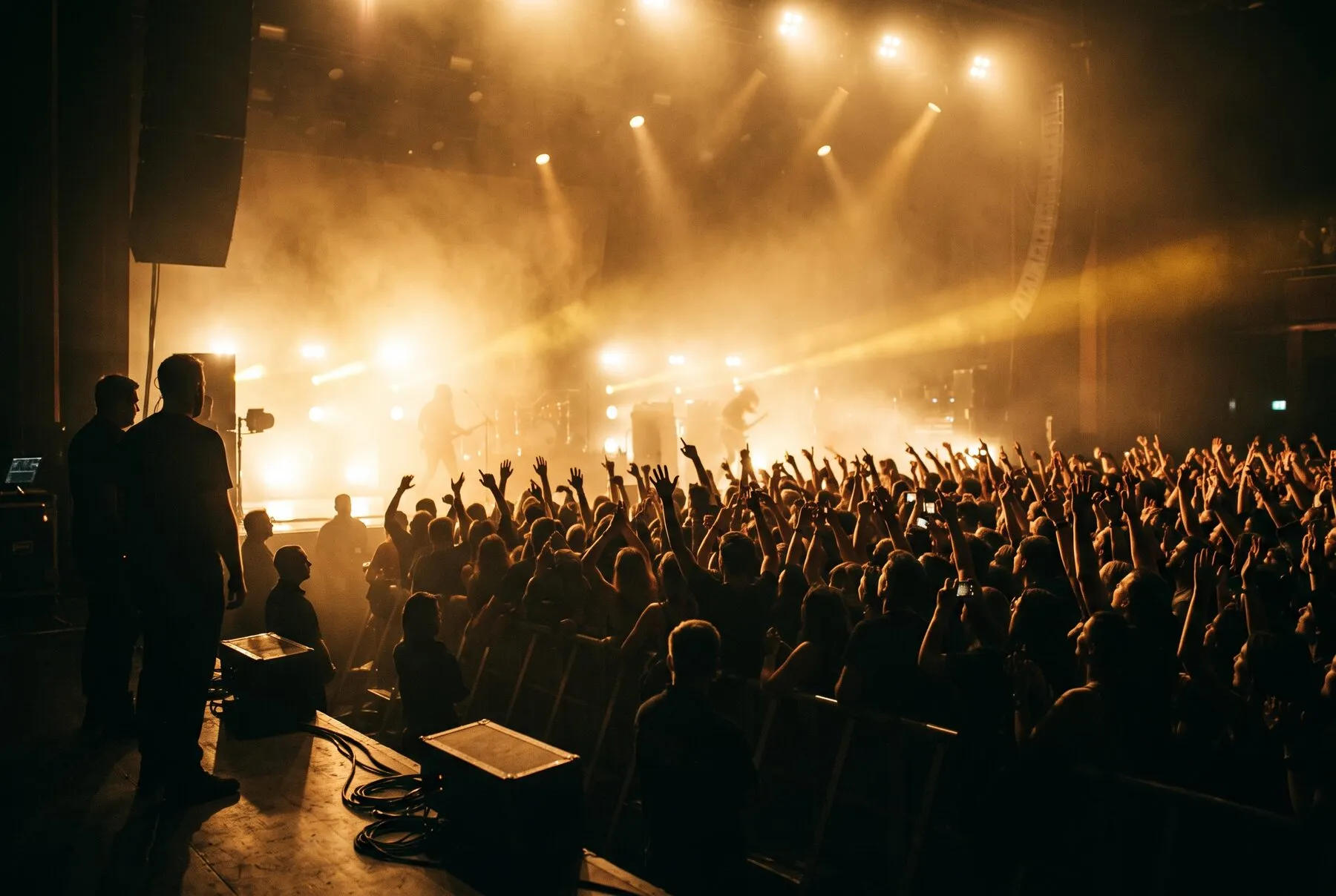A concert crowd with raised hands silhouetted against golden stage lights